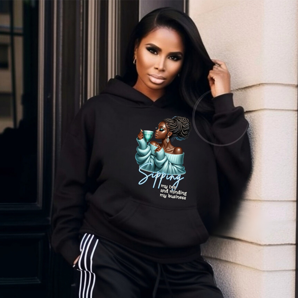 Woman wearing a black hoodie with a graphic design and text, leaning against a wall.