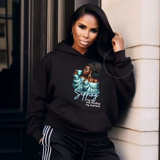 Woman wearing a black hoodie with a graphic design and text, leaning against a wall.