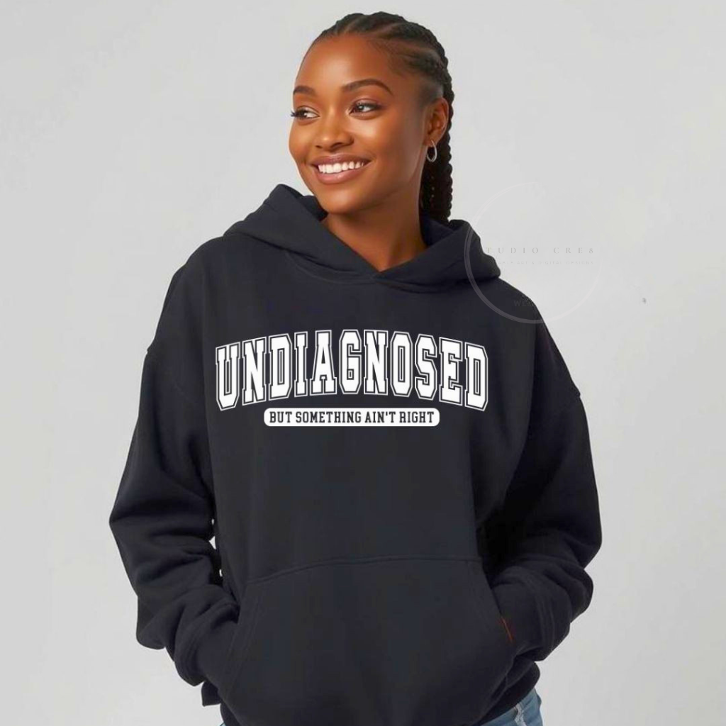 Person wearing a black hoodie with 'undiagnosed but something ain't right' text on a plain background