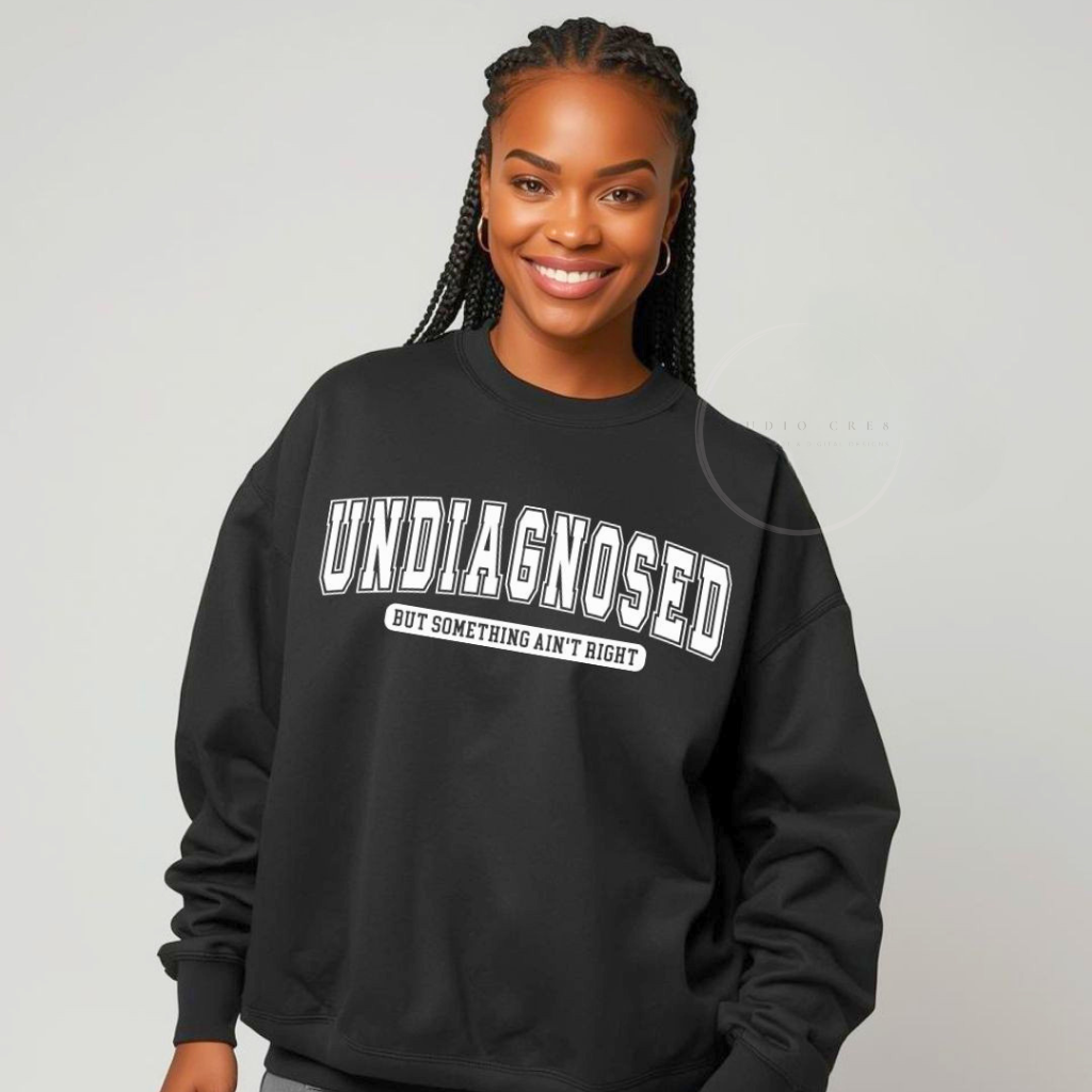 Person wearing a black sweatshirt with 'undiagnosed but something ain't right' text on a plain background