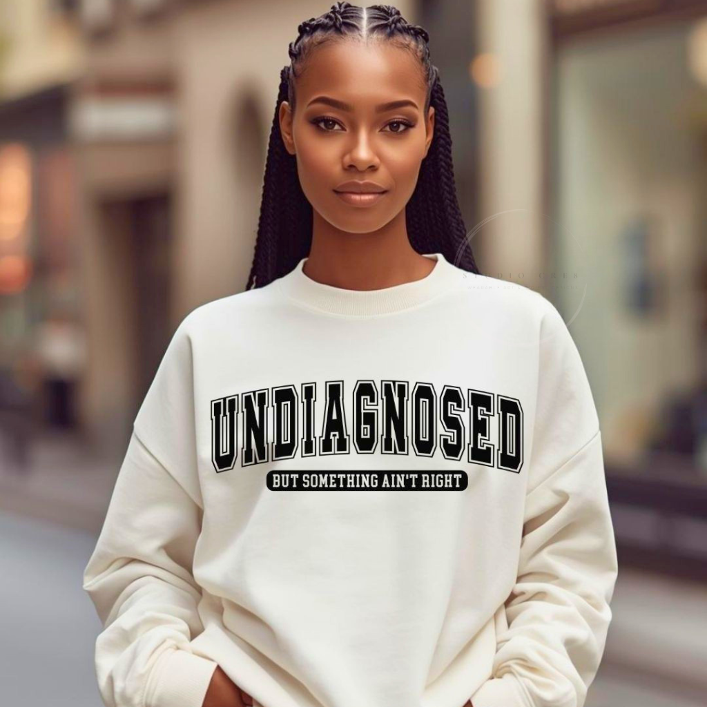 Person wearing a white sweatshirt with 'undiagnosed but something ain't right' text on a blurred street background
